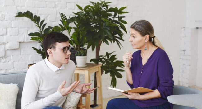 psychology-therapy-psychiatry-mental-health-counseling-concept-candid-shot-nervous-self-conscious-young-male-glasses-telling-middle-aged-female-counselor-about-his-problems-work